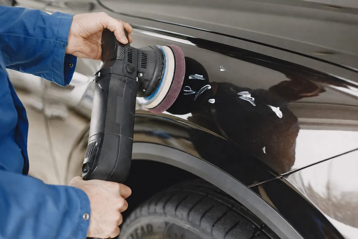 A detailer machine-polishing a dark car panel during paint correction
